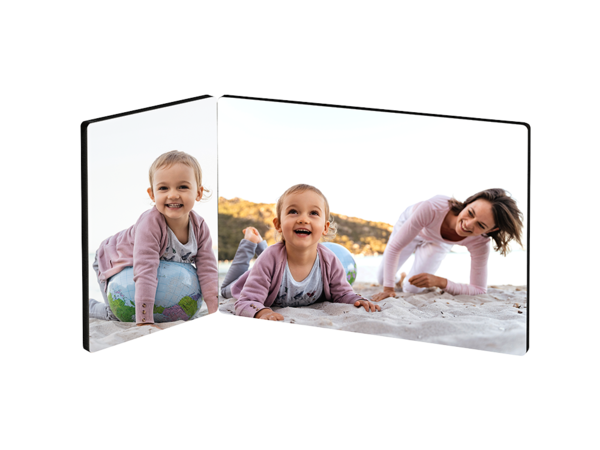 Ein zweiteiliger Fotoaufsteller zeigt eine fröhliche Szene am Strand. Auf der linken Seite sitzt ein kleines Mädchen auf einem bunten Ball und lächelt.